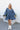 Full body front view of model wearing the Away We Go Dress, that has blue washed fabric, a two-tiered babydoll style, a v neckline, and 3/4 balloon sleeves with elastic wrists.