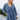 Front view of model wearing the Away We Go Dress, that has blue washed fabric, a two-tiered babydoll style, a v neckline, and 3/4 balloon sleeves with elastic wrists.