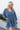 Front view of model wearing the Away We Go Dress, that has blue washed fabric, a two-tiered babydoll style, a v neckline, and 3/4 balloon sleeves with elastic wrists.