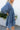 Side view of model wearing the Away We Go Dress, that has blue washed fabric, a two-tiered babydoll style, a v neckline, and 3/4 balloon sleeves with elastic wrists.