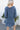 Back view of model wearing the Away We Go Dress, that has blue washed fabric, a two-tiered babydoll style, a v neckline, and 3/4 balloon sleeves with elastic wrists.