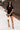 Full body front view of model wearing the Running The Show Denim Romper, which features black washed denim, a surplice neck that snaps with a collar, half-length sleeves, a front zipper, pockets, pleating on the legs, and a 3" inseam