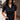 Front view of model wearing the Running The Show Denim Romper, which features black washed denim, a surplice neck that snaps with a collar, half-length sleeves, a front zipper, pockets, pleating on the legs, and a 3" inseam