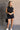 Full body view of model wearing the Emily Washed Black Denim Sleeveless Romper which features washed black denim fabric, two front pockets, silver button details, button up front closure, two front chest buttoned pockets, two back pockets, collared neckli