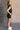 Full body side view of model wearing the Emily Washed Black Denim Sleeveless Romper which features washed black denim fabric, two front pockets, silver button details, button up front closure, two front chest buttoned pockets, two back pockets, collared n