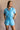 Front view of model wearing the Delilah Washed Sky Blue Short Sleeve Romper which features washed light blue tencel fabric, two front slit pockets, an elastic waistband with a drawstring tie, a right front chest pocket, tortoise button closures, a collare