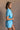 Side view of model wearing the Delilah Washed Sky Blue Short Sleeve Romper which features washed light blue tencel fabric, two front slit pockets, an elastic waistband with a drawstring tie, a right front chest pocket, tortoise button closures, a collared