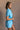 Side view of model wearing the Delilah Washed Sky Blue Short Sleeve Romper which features washed light blue tencel fabric, two front slit pockets, an elastic waistband with a drawstring tie, a right front chest pocket, tortoise button closures, a collared