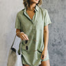 Front view of model wearing the Aubrie Washed Olive Short Sleeve Mini Dress which features washed olive tencel fabric, one front chest pocket, a hidden quarter button-up, a v neckline with a collar, a frayed mini-length hem, and cuffed short sleeves.