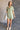 Full body view of model wearing the Aubrie Washed Olive Short Sleeve Mini Dress which features washed olive tencel fabric, one front chest pocket, a hidden quarter button-up, a v neckline with a collar, a frayed mini-length hem, and cuffed short sleeves.