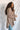 Close-up side view of model wearing the Easy Breezy Top, that has a mocha colored knit material, an open knit design, a V neckline, a long cuffed sleeve, side slits, and a high-low design.