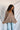 Back view of model wearing the Easy Breezy Top, that has a mocha colored knit material, an open knit design, a V neckline, a long cuffed sleeve, side slits, and a high-low design.