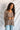 Back view of model wearing the Easy Breezy Top, that has a mocha colored knit material, an open knit design, a V neckline, a long cuffed sleeve, side slits, and a high-low design.