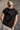Back view of model wearing the Presley Black Sleeveless Hoodie Sweatshirt which features black knit fabric, monochrome quarter zip up, high neckline, hoodie attached with drawstring details, one front pocket and sleeveless.
