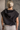 Back view of model wearing the Presley Black Sleeveless Hoodie Sweatshirt which features black knit fabric, monochrome quarter zip up, high neckline, hoodie attached with drawstring details, one front pocket and sleeveless.