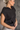 Side view of model wearing the Presley Black Sleeveless Hoodie Sweatshirt which features black knit fabric, monochrome quarter zip up, high neckline, hoodie attached with drawstring details, one front pocket and sleeveless.