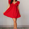 Full body view of model wearing the Aurora Red Floral Ruffle Mini Dress which features red fabric with a brown 3d floral pattern, a mini-length baby doll style, a v neckline, elastic straps with ruffles, and an open back with a bow detail.