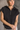 Front view of model wearing the Presley Black Sleeveless Hoodie Sweatshirt which features black knit fabric, monochrome quarter zip up, high neckline, hoodie attached with drawstring details, one front pocket and sleeveless.