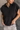 Close up view of model wearing the Presley Black Sleeveless Hoodie Sweatshirt which features black knit fabric, monochrome quarter zip up, high neckline, hoodie attached with drawstring details, one front pocket and sleeveless.