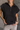 Close up view of model wearing the Presley Black Sleeveless Hoodie Sweatshirt which features black knit fabric, monochrome quarter zip up, high neckline, hoodie attached with drawstring details, one front pocket and sleeveless.