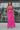Full body front view of model wearing the Coastal Paradise Dress in Pink that has hot pink ribbed fabric, midi length, a round neckline, an elastic waistband, and spaghetti straps. Styled with gold belt.