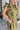 Side view of the Meet Your Match Dress that features a green colored material, a collar neckline, a button-up front, a ruffle sleeve, side pockets, and a mini length.