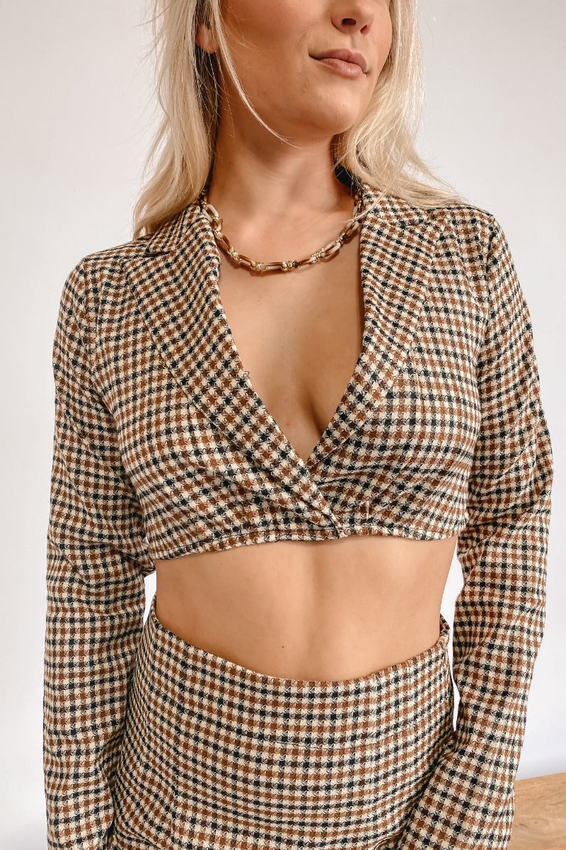 Frontal view of the It Takes Two Crop Blazer that features a beige colored tweed material, a brown and black gingham print, a collar and lapel neckline, a long sleeve, and a cropped fit.