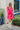 Frontal view of the Wide Open Spaces Mini Dress that features a hot pink material, a round neck with a ruffle trim, a 3/4 button-up front, a long sleeve, a tiered babydoll design, and a flowy fit.