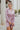 Frontal view of the Risk It All Dress that features a dusty pink silk material, a collar neck, a V surplice neckline, a long cuffed sleeve, a wrap front with a tie detail, and a mini length.