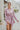 Frontal view of the Risk It All Dress that features a dusty pink silk material, a collar neck, a V surplice neckline, a long cuffed sleeve, a wrap front with a tie detail, and a mini length.