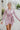 Frontal view of the Risk It All Dress that features a dusty pink silk material, a collar neck, a V surplice neckline, a long cuffed sleeve, a wrap front with a tie detail, and a mini length.