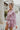 Side view of the Risk It All Dress that features a dusty pink silk material, a collar neck, a V surplice neckline, a long cuffed sleeve, a wrap front with a tie detail, and a mini length.