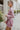Side view of the Risk It All Dress that features a dusty pink silk material, a collar neck, a V surplice neckline, a long cuffed sleeve, a wrap front with a tie detail, and a mini length.