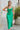 Frontal view of the Call You Mine Midi Dress In Green that features a green colored silk material, a cowl neckline, a sleeveless design with thin adjustable straps, a side slit, and a midi length.