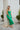 Frontal view of the Call You Mine Midi Dress In Green that features a green colored silk material, a cowl neckline, a sleeveless design with thin adjustable straps, a side slit, and a midi length.