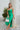 Frontal view of the Call You Mine Midi Dress In Green that features a green colored silk material, a cowl neckline, a sleeveless design with thin adjustable straps, a side slit, and a midi length.