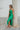 Side view of the Call You Mine Midi Dress In Green that features a green colored silk material, a cowl neckline, a sleeveless design with thin adjustable straps, a side slit, and a midi length.