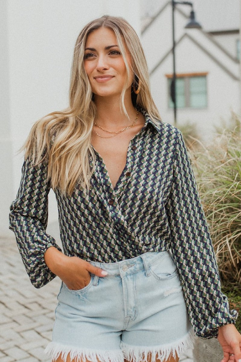 Frontal view of the Around The Block Top that features a navy chiffon material, a taupe and green geometric print, a collar neckline, a button-up front, and a long sleeve.