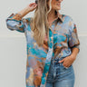Frontal view of the Signature Move Top that features a multi-colored silk material with a watercolor design, a collar neck, long cuffed sleeves, a button-up front, and a front pocket.