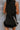 Back detail view of model wearing The Midnight Magic Feather Dress features black fabric, a mock neckline, a sleeveless a-line silhouette, and a feather-trimmed hemline.
