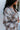 Side view of model wearing the Coffee Date Plaid Shacket, that has a white, taupe, rust, and blue plaid print, a button front with a collar, tortoise buttons, 2 front chest pockets, and long sleeves. Worn over a white brami.