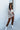 Full body front view of model wearing the Coffee Date Plaid Shacket, that has a white, taupe, rust, and blue plaid print, a button front with a collar, tortoise buttons, 2 front chest pockets, and long sleeves. Worn over a white brami.