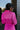 Back view of model wearing the Dancing Queen Dress, that has a fuchsia textured material, a satin collar neck, a button-up front, long cuffed sleeves, an adjustable tie belt, and lettuce edge bottom hem.
