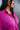 Close-up front view of model wearing the Dancing Queen Dress, that has a fuchsia textured material, a satin collar neck, a button-up front, long cuffed sleeves, an adjustable tie belt, and lettuce edge bottom hem.