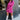 Full body front view of model wearing the Dancing Queen Dress, that has a fuchsia textured material, a satin collar neck, a button-up front, long cuffed sleeves, an adjustable tie belt, and lettuce edge bottom hem.