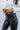 Close-up frontal view of 5'8 model wearing the Next Level Straight Leg Pants features a black faux-leather material, a high-rise fit, a clasp and zipper front closure, belt loops, two front pockets, a middle seam down the legs, and a straight leg fit