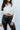 Front view of model wearing the On Your Own Top, which features an off white material, a collar neck, a surplice neckline, long cuffed sleeves, a draped knot detail at the front hem, and a ruched elastic back bottom hem.
