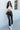 Full body front view of 5'8 model wearing the Next Level Straight Leg Pants features a black faux-leather material, a high-rise fit, a clasp and zipper front closure, belt loops, two front pockets, a middle seam down the legs, and a straight leg fit