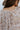 Close-up back view of model wearing the Ever After Floral Top, which features mocha-colored fabric with white, blue, and rust floral print, a notched v-neckline, long sleeves with elastic wrists, and a flowy fit.