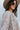 Close-up side view of model wearing the Ever After Floral Top, which features mocha-colored fabric with white, blue, and rust floral print, a notched v-neckline, long sleeves with elastic wrists, and a flowy fit.